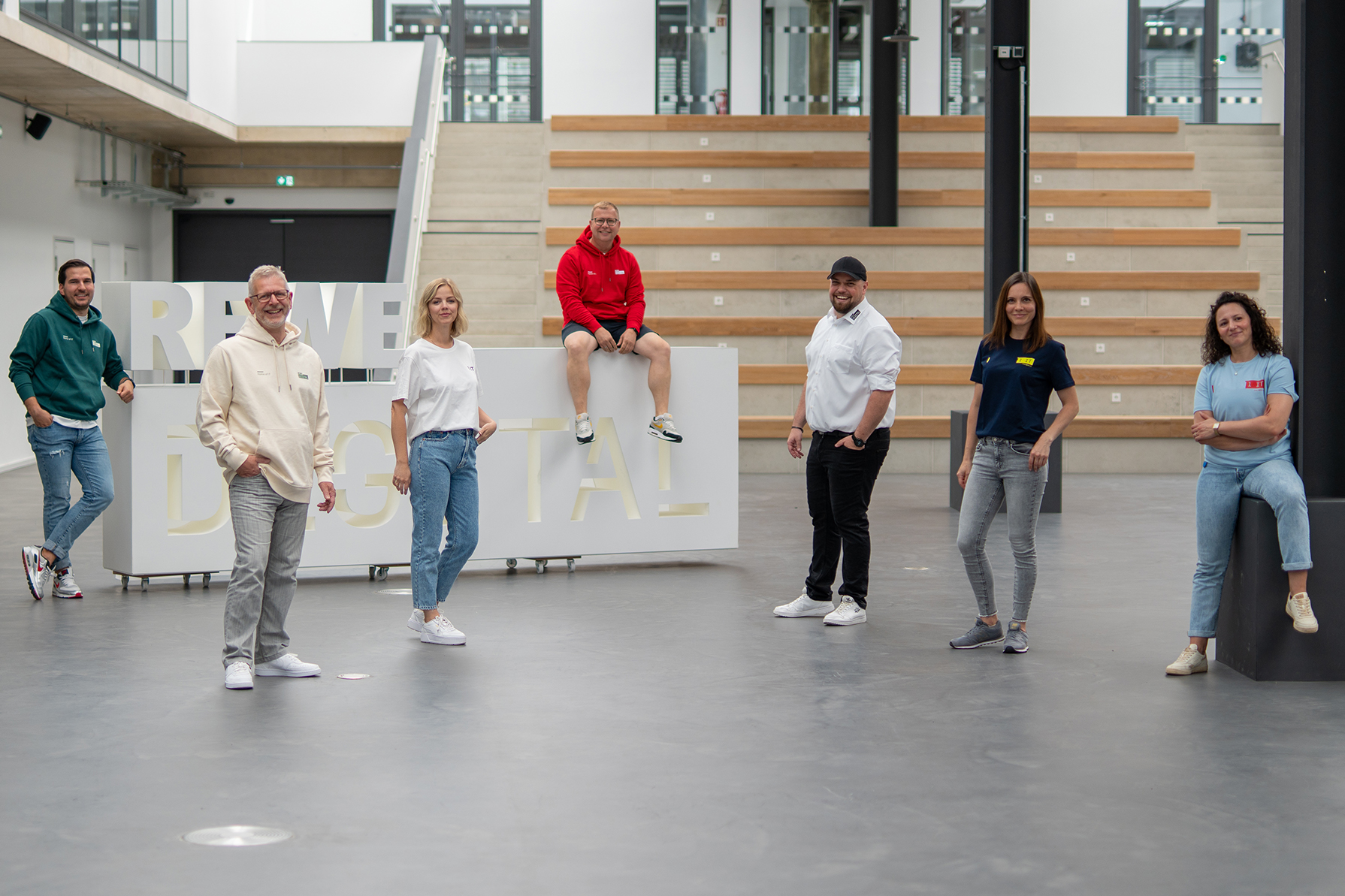 REWE digital Team in Merch vor dem REWE digital Schriftzug im Atrium