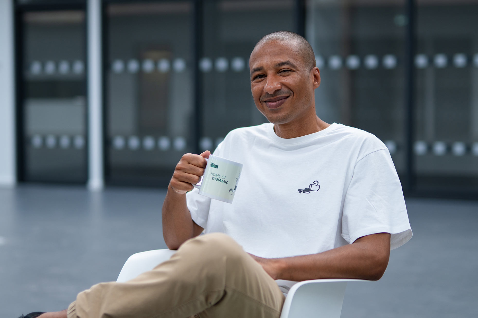 Kollege im weißen REWE digital T-Shirt mit Tasse im Büro