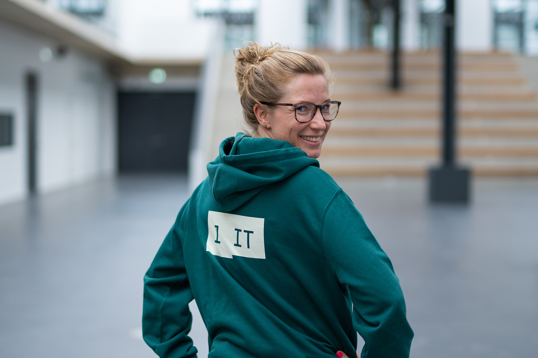 REWE digital Mitarbeiterin im grünen Hoodie mit 1 IT Print im Foyer